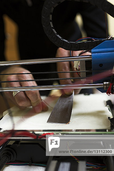 Abgetrennte Hände eines männlichen Ingenieurs beim Fixieren eines 3D-Druckers auf dem Tisch