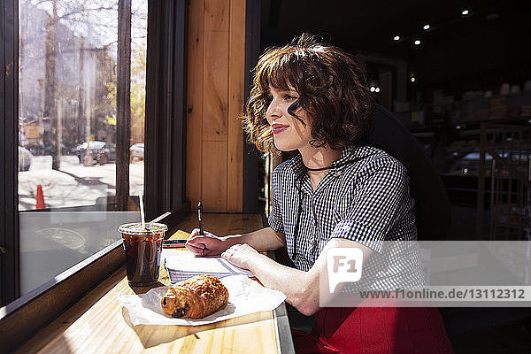 Frau schaut durchs Fenster  während sie im Café sitzt