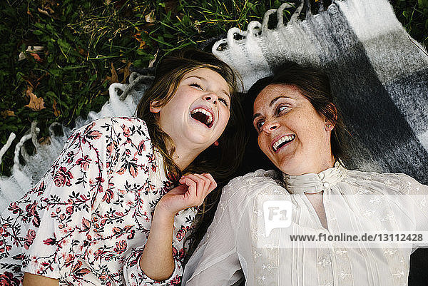 High angle view of cheerful mother and daughter lying on picnic blanket at park