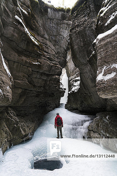 Rear view of hiker with backpack standing on frozen stream amidst mountains