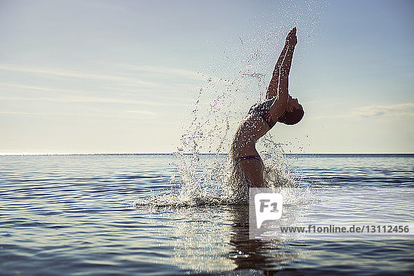 Verführerische Frau  die Wasser spritzt  während sie gegen den Himmel ins Meer taucht