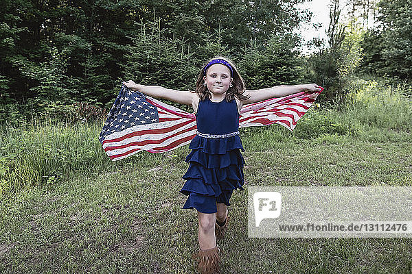 Portrait of smiling girl holding American flag while walking on grassy field