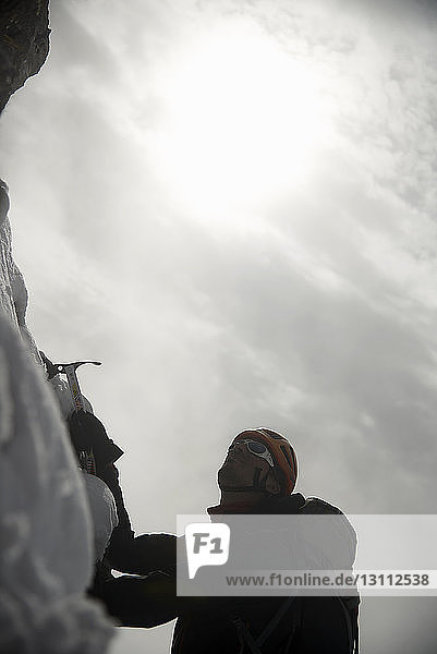 Niedrigwinkelansicht eines Wanderers mit Eispickel  der im Winter beim Klettern den Berg gegen den Himmel benutzt