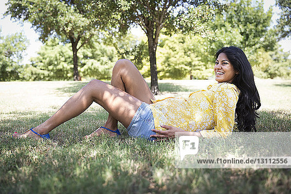 Glückliche schwangere Frau liegt auf Gras im Park