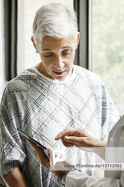 Ausgeschnittenes Bild eines Arztes  der dem Patienten einen medizinischen Bericht auf einem digitalen Tablett in der Klinik zeigt