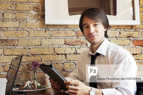 Portrait of businessman holding tablet computer in cafe