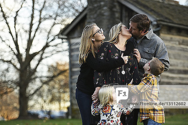 Parents kissing while standing with children at yard