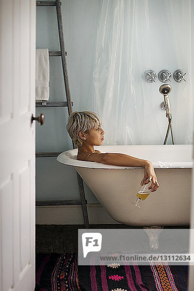 Seitenansicht einer nachdenklichen Frau  die beim Entspannen zu Hause in der Badewanne ein Trinkglas hält