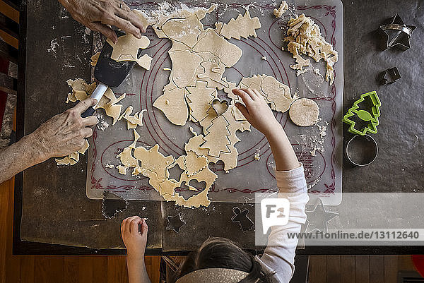 Overhead view of granddaughter helping grandmother in making Christmas cookies on table at home