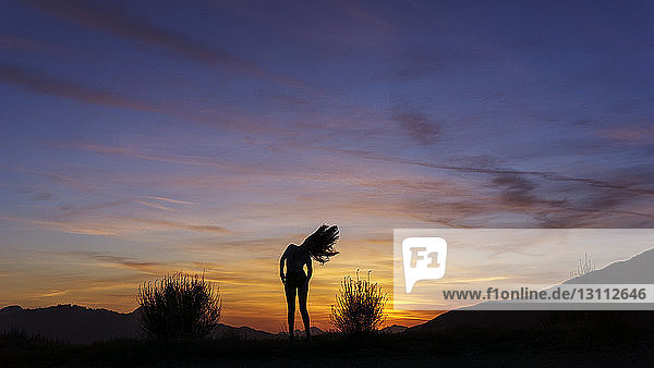 Silhouettenfrau  die bei Sonnenuntergang auf dem Feld steht und mit den Haaren wackelt