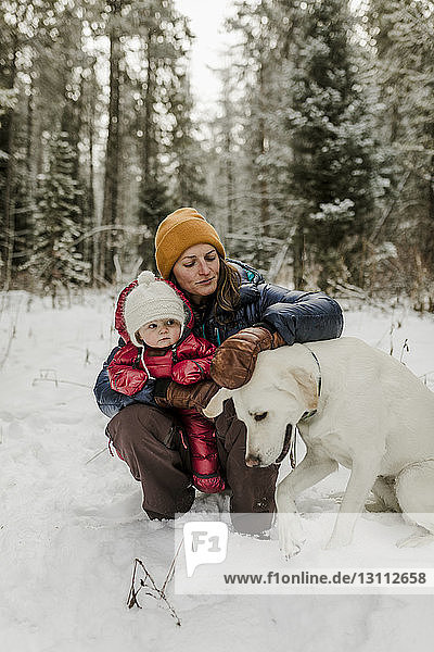 Mutter mit Tochter streichelnder Hund im Wald im Winter