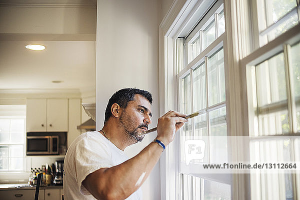 Seitenansicht eines Mannes  der zu Hause Fensterrahmen malt