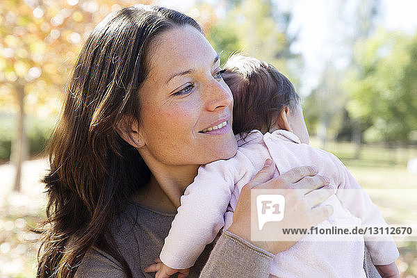 Smiling mother carrying toddler while standing at park
