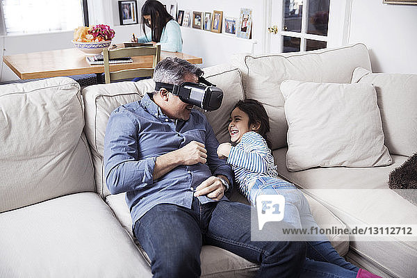 Playful father wearing virtual reality simulator while playing with daughter at home