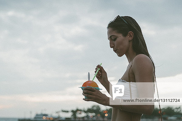 Seitenansicht einer Frau  die Wüste isst  während sie vor bewölktem Himmel steht