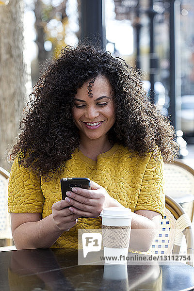 Lächelnde Frau benutzt Smartphone  während sie in einem Straßencafé in der Stadt sitzt