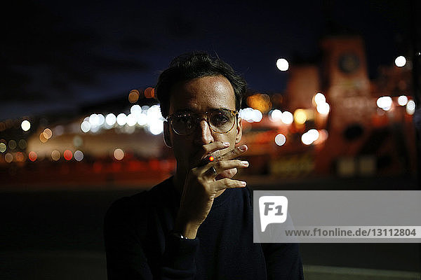 Portrait of man smoking while standing on street at night