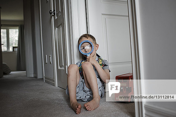 Junge blickt durch eine Lupe  während er zu Hause an der Tür sitzt