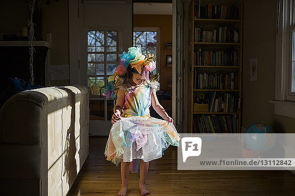 Mädchen in voller Länge in farbenfrohem Einhorn-Kostüm  das zu Hause auf Hartholzboden steht