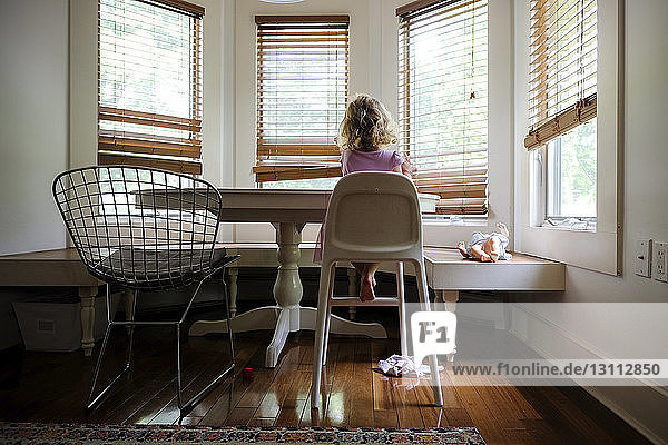 Rear view of girl sitting on high chair by table at home
