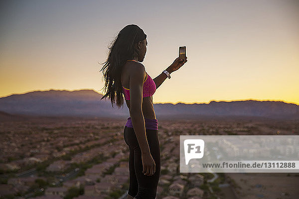 Sportswoman photographing through mobile phone during sunset
