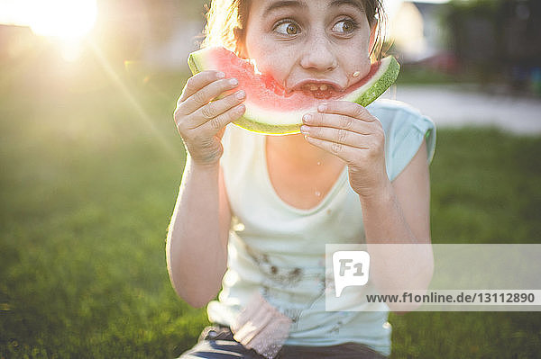 Mädchen isst Wassermelone  während sie auf einem Grasfeld sitzt