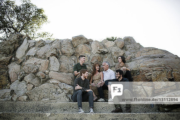 Fröhliche Familie redet  während sie bei Felsformationen vor dem klaren Himmel im Park sitzt