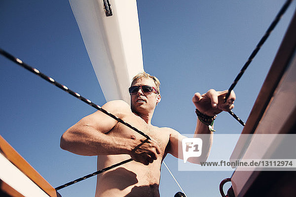 Low angle view of man pulling ropes on boat against clear blue sky