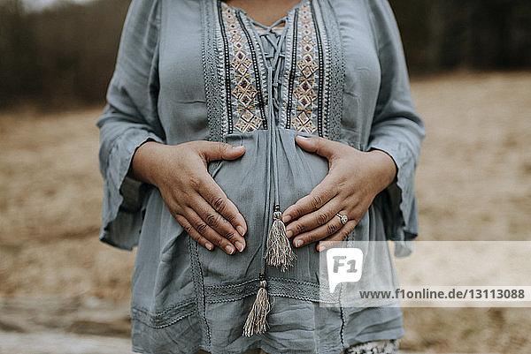 Mittendrin einer schwangeren Frau  die den Bauch berührt  während sie im Wald steht