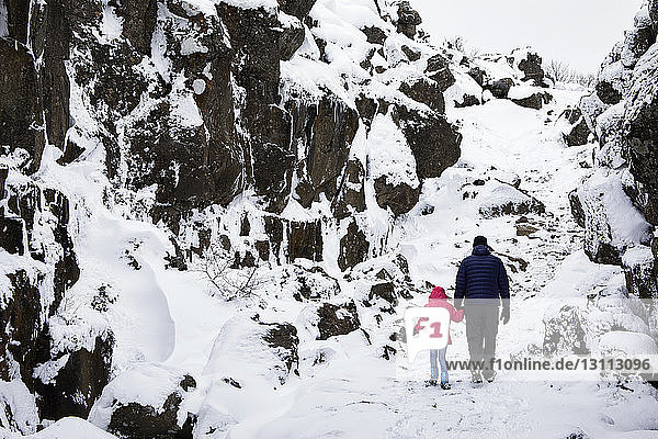 Rückansicht von Vater und Tochter beim Spaziergang zwischen schneebedeckten Felsen