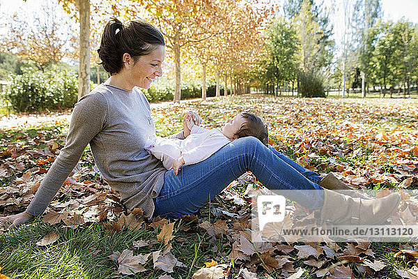 Smiling mother playing with toddler at park during autumn