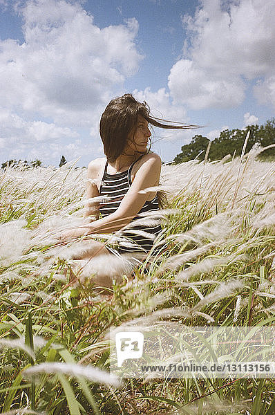 Frau sitzt bei windigem Wetter auf dem Feld gegen den Himmel