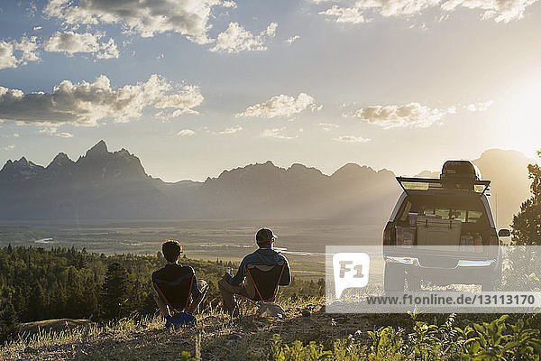 Rear view of male hikers relaxing on reclining chair in field
