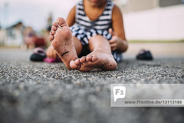 Niedrige Sektion eines Mädchens mit unordentlichen Füßen auf der Straße sitzend