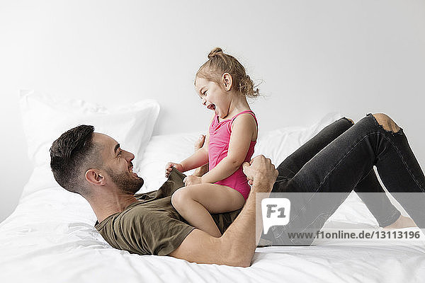 Seitenansicht eines glücklichen Vaters  der mit seiner Tochter spielt  während er zu Hause im Bett liegt