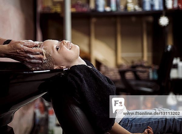 Geschnittene Hände eines Friseurs  der im Salon Mädchen die Haare wäscht