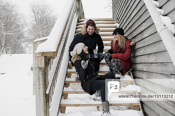 Happy friends talking while sitting on snow covered steps