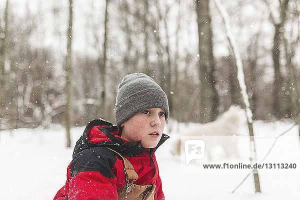 Side view of teenage boy looking away while standing in forest during winter