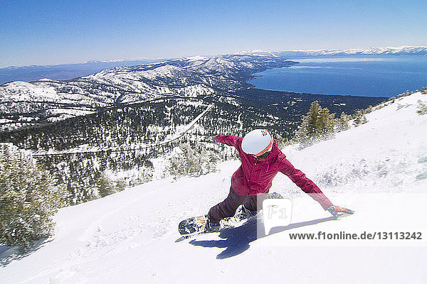 Hochwinkelaufnahme einer Snowboarderin beim Abstieg vom schneebedeckten Berg