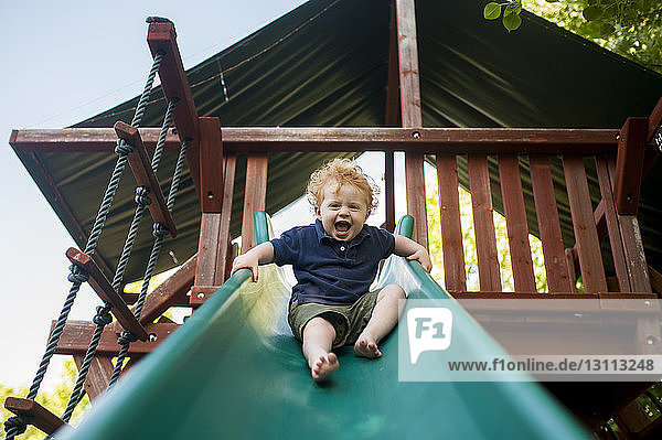 Low angle portrait of happy baby boy screaming while sliding at yard