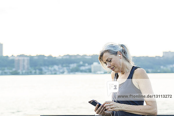 Woman using smart phone while listening music on bridge against clear sky