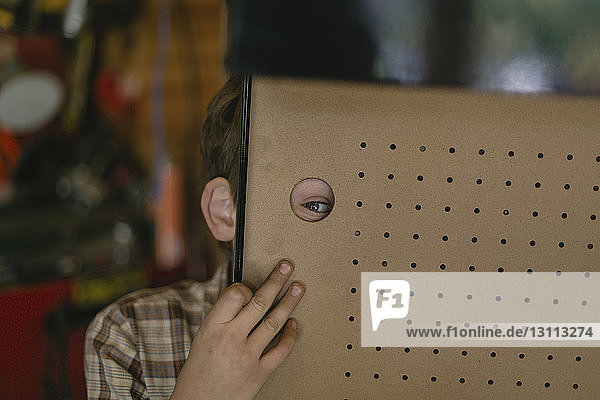 Porträt eines verspielten Jungen  der durch ein Loch im Karton schaut