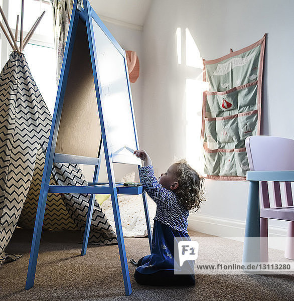 Girl writing on artist's canvas while sitting on rug at home