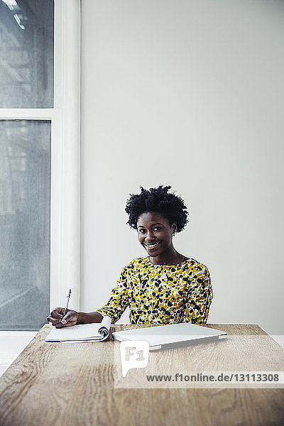 Porträt einer glücklichen Geschäftsfrau  die am Schreibtisch im Sitzungssaal schreibt