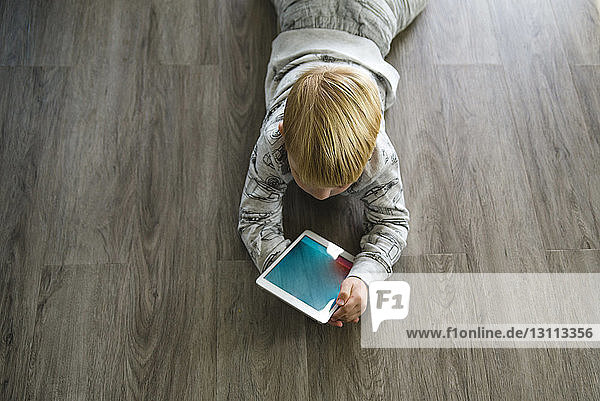 High angle view of boy using tablet computer while lying on floor at home