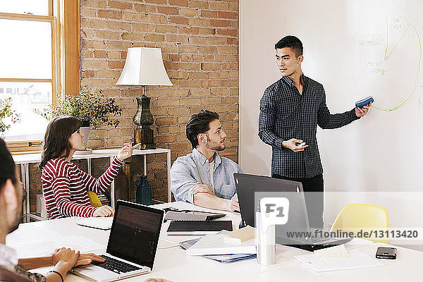 Colleagues looking at businessman explaining plan on whiteboard during meeting in boardroom