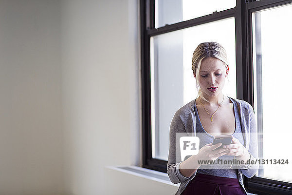 Businesswoman using mobile phone by window in new office