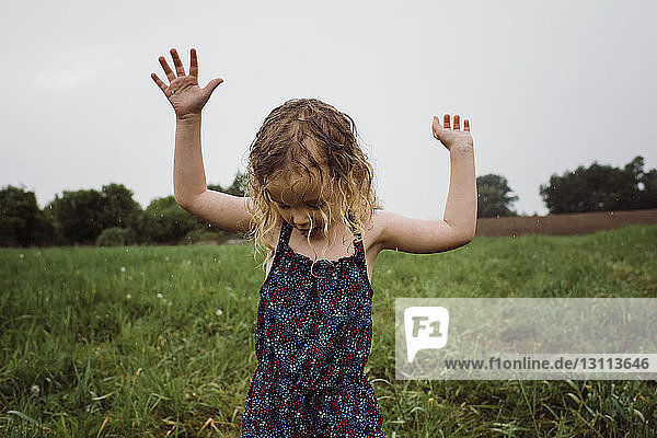 Feuchtes Mädchen mit erhobenen Armen auf Grasfeld stehend gegen den Himmel im Park während der Regenzeit