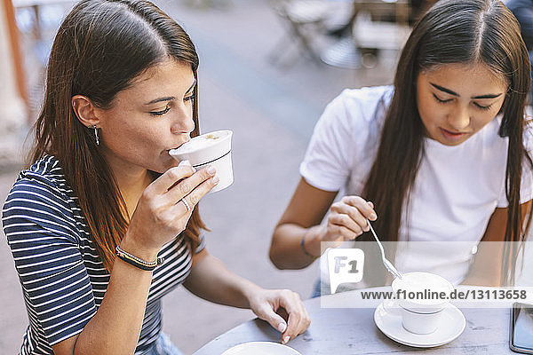 Schrägaufnahme von Freunden  die Cappuccino trinken  während sie im Straßencafé sitzen