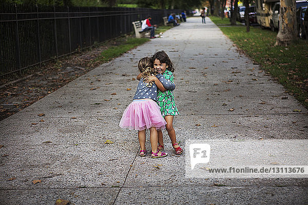 Fröhliche Schwestern umarmen sich auf dem Fußweg im Park